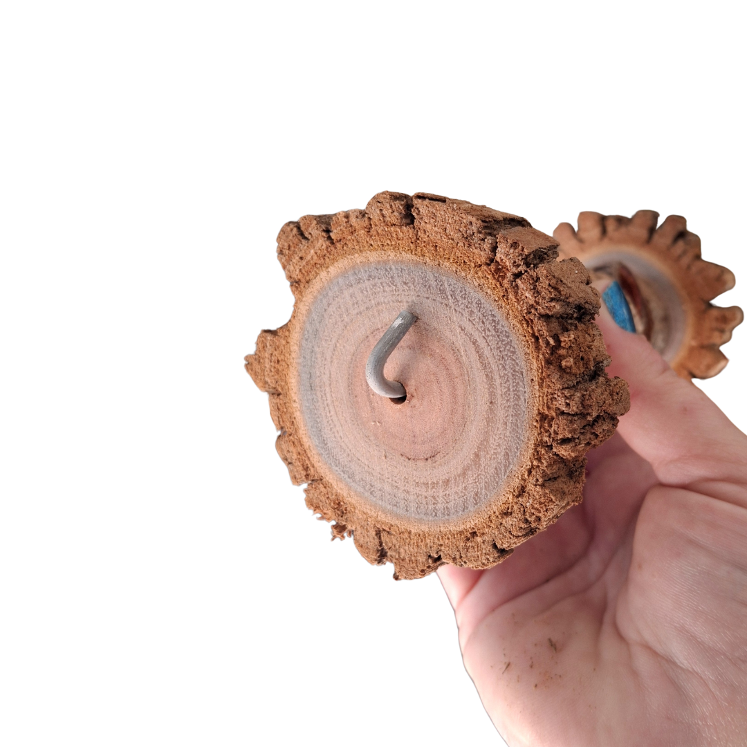 Hand holding a wooden dumbbell bird toy with a metal hook on a white background